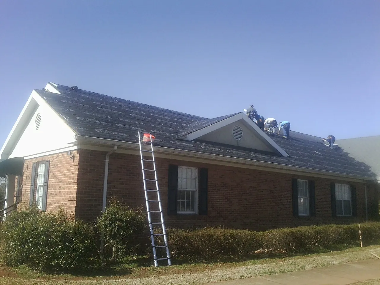 Crew tearing shingles off a brick ranch roof with a ladder set — Emergency Roof Repair work by our crew in Kempton