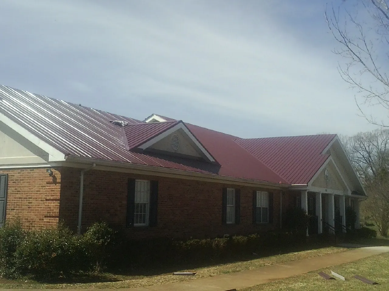 Red metal roof with gabled entries on a long brick building, from a Hail Damage Roof Repair job in Kempton