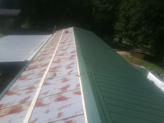 Old rusted panels beside newly installed green metal roofing — Wind Damage Roof Repair by Roofing Brothers in Kempton
