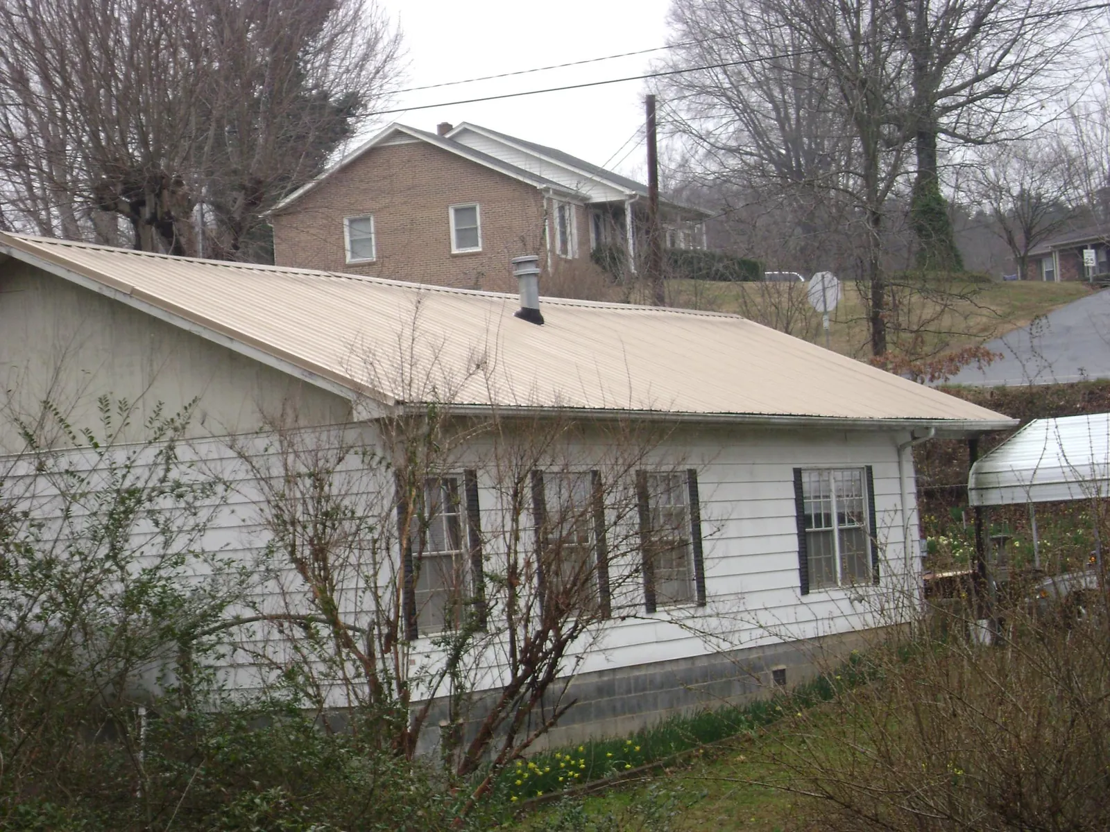 Tan metal roof on a white sided house set into a hillside — Commercial Roofing by Roofing Brothers in Kempton